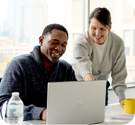 Two coworkers happily collaborating in a conference room on a laptop.
