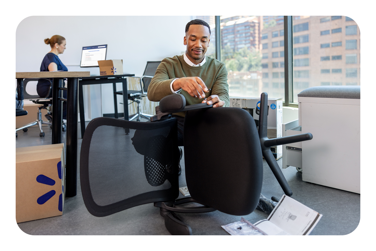 Picture of a man wearing a sweater putting together a chair in an office.